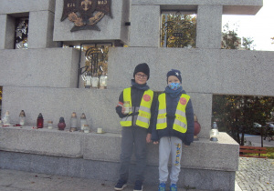 Mateusz i Bartek stawiają znicze pod pomnikiem Harcerzy